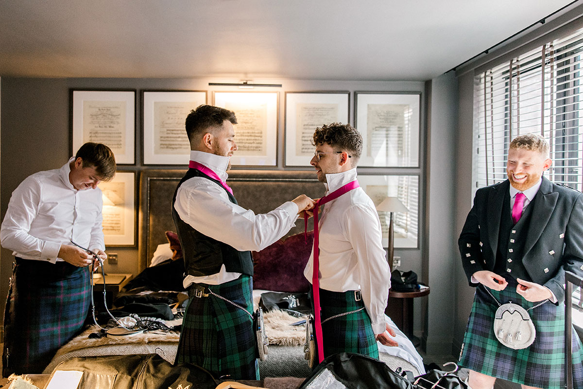 Groomsmen helping each other get ready while adjusting ties and jackets before the ceremony