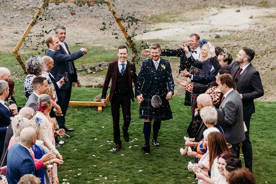 Two grooms walk through two lines of guests throwing confetti
