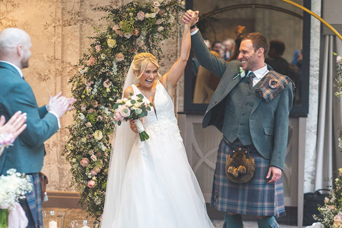 bride and groom hold hands and raise their arms in the air at the altar