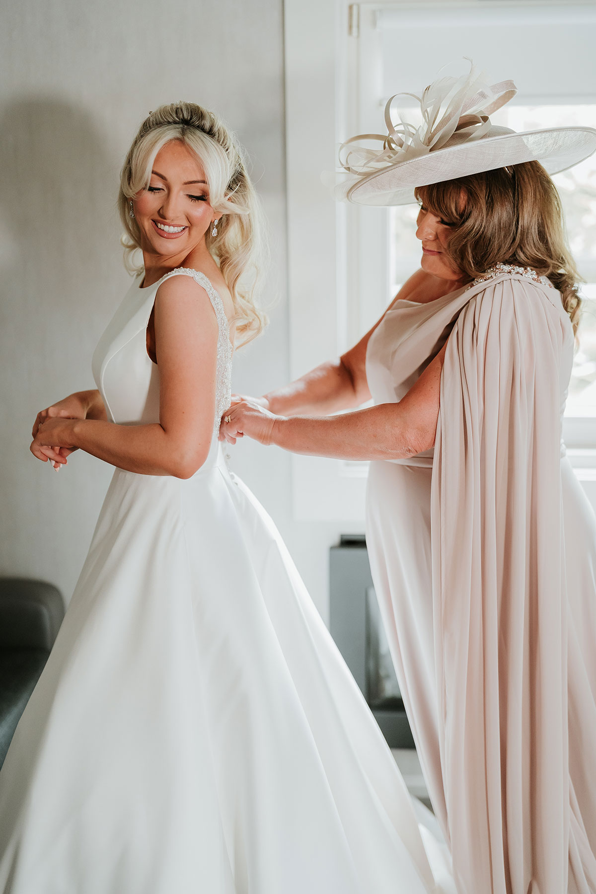 Bride getting ready as mother fastens wedding dress at Ingliston Country Club