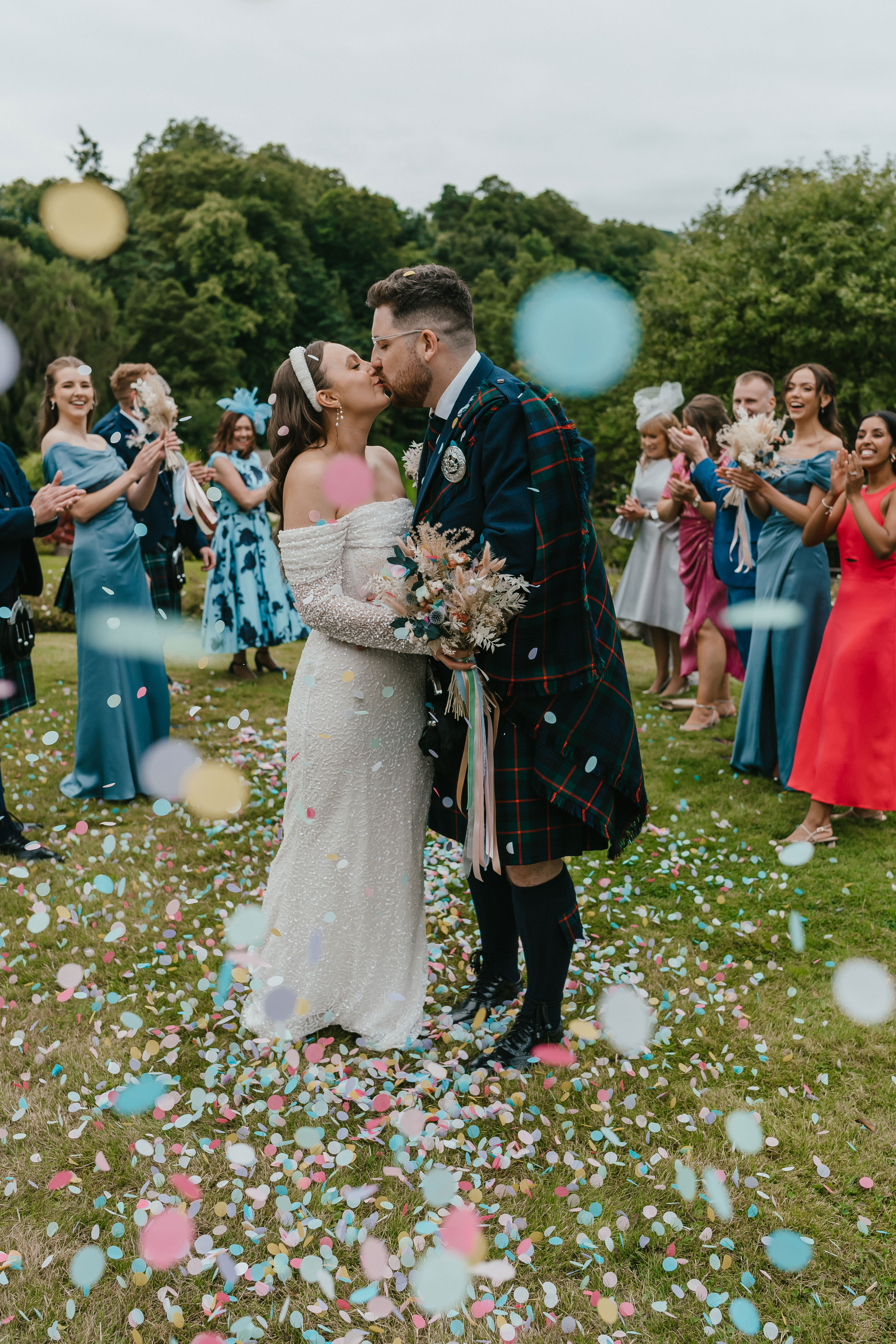 bride and groom kiss as guests throw confetti over them during wedding at Robert Burns birth place