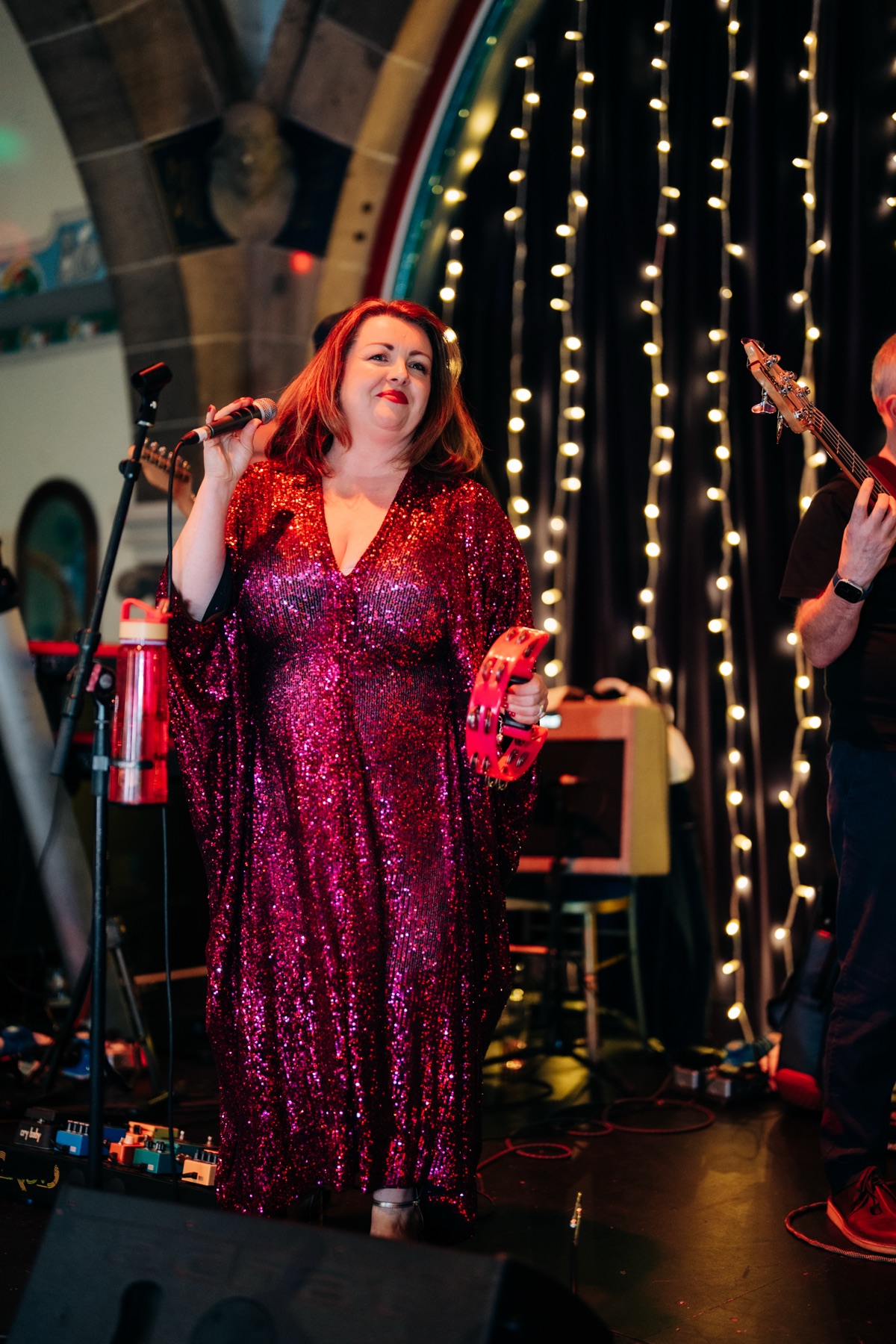 Singer performs at Robyn and James's wedding reception at Òran Mór in Glasgow, wearing a red sequinned dress and holding a tambourine.