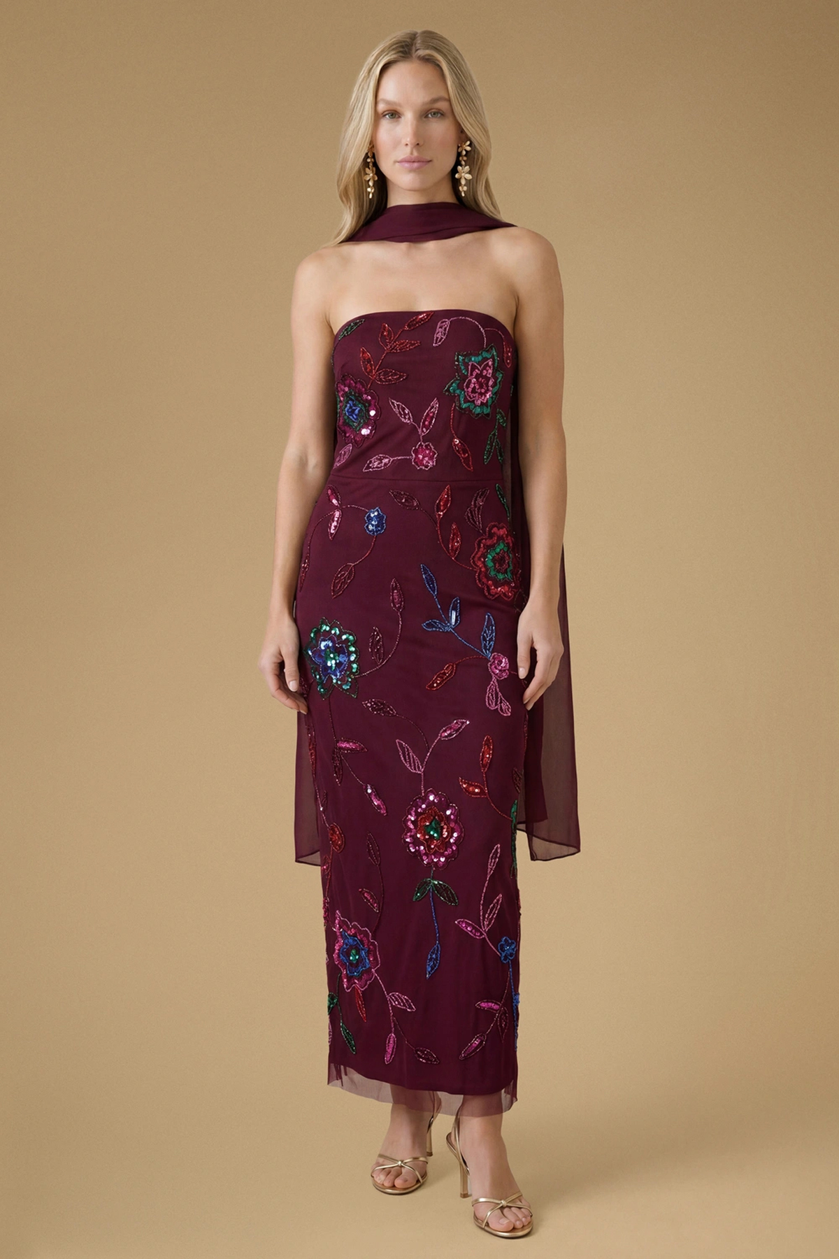 Woman wearing a burgundy strapless midaxi dress with colourful floral embroidery, sequins and a matching chiffon scarf.