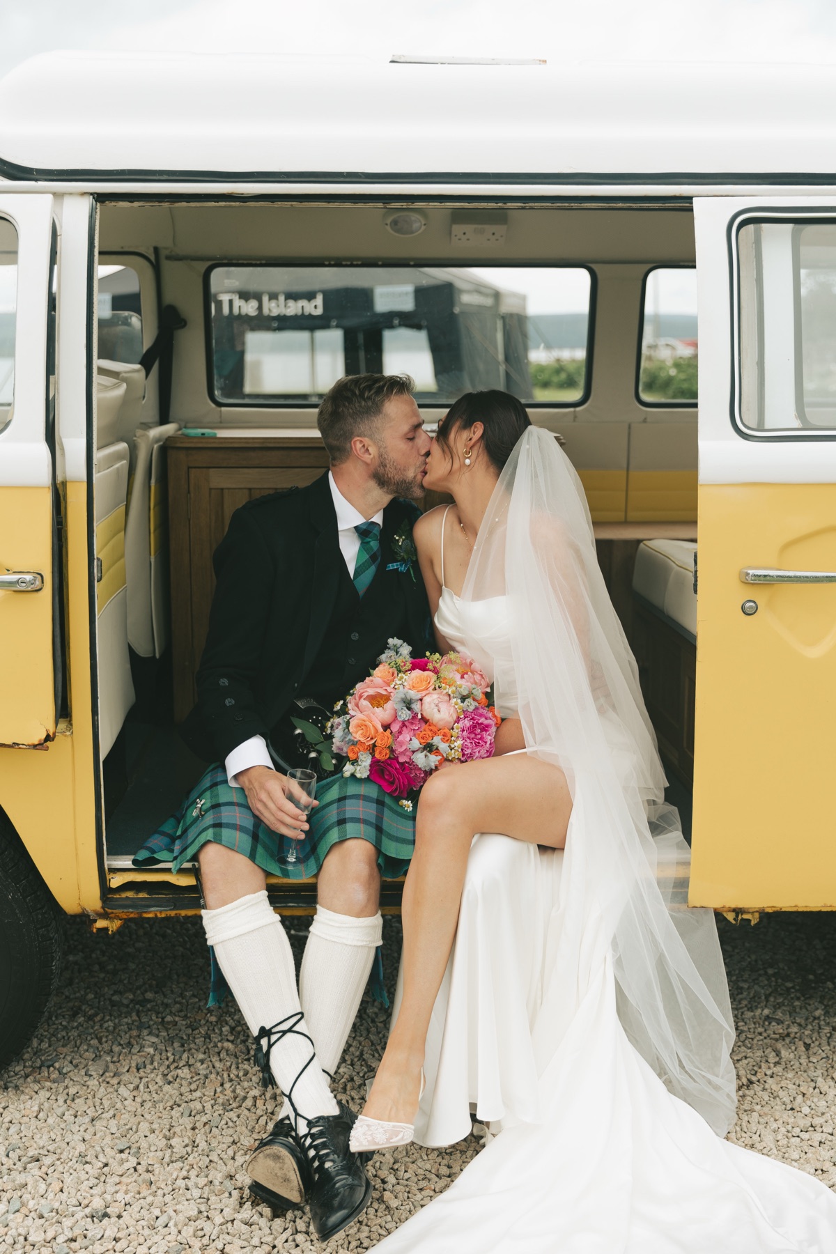 Gary and Isobel kiss in the doorway of a yellow vintage VW campervan during their wedding portraits on Arran.