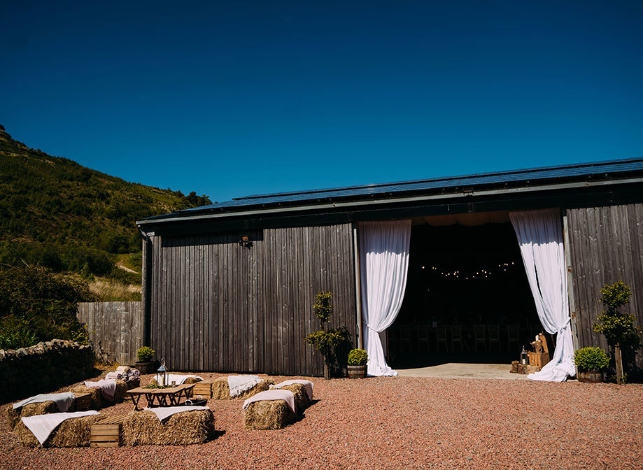 outside of a barn on a sunny day with white curtains over the entrance 