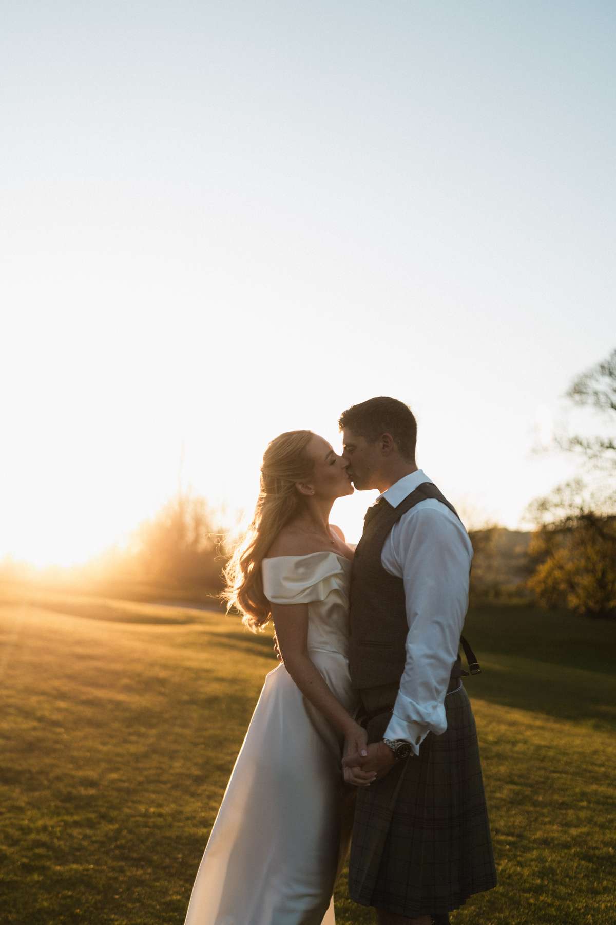 Siân and Stuart kiss at sunset in the grounds of Mar Hall, with the bride in Vivienne Westwood and groom in a kilt.