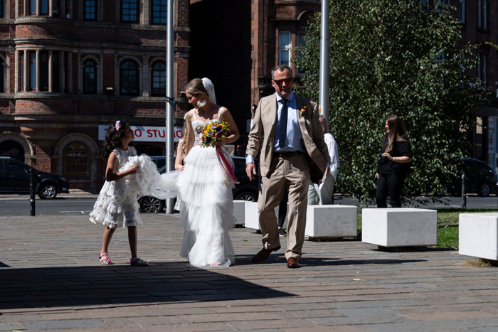 Flower girl helps carry the bride's veil as she walks to the venue