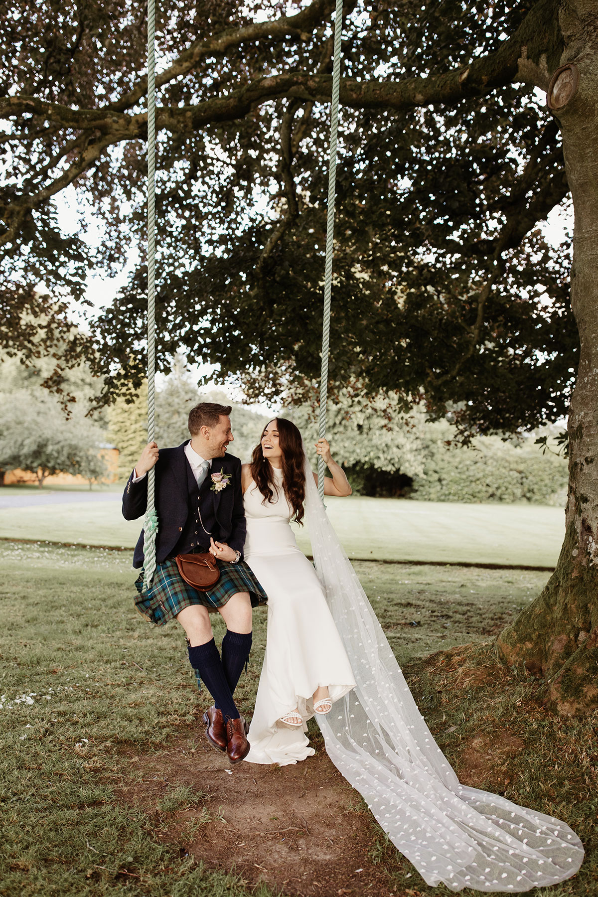 a bride and groom on a swing below at tree in the grounds of Netherdale House