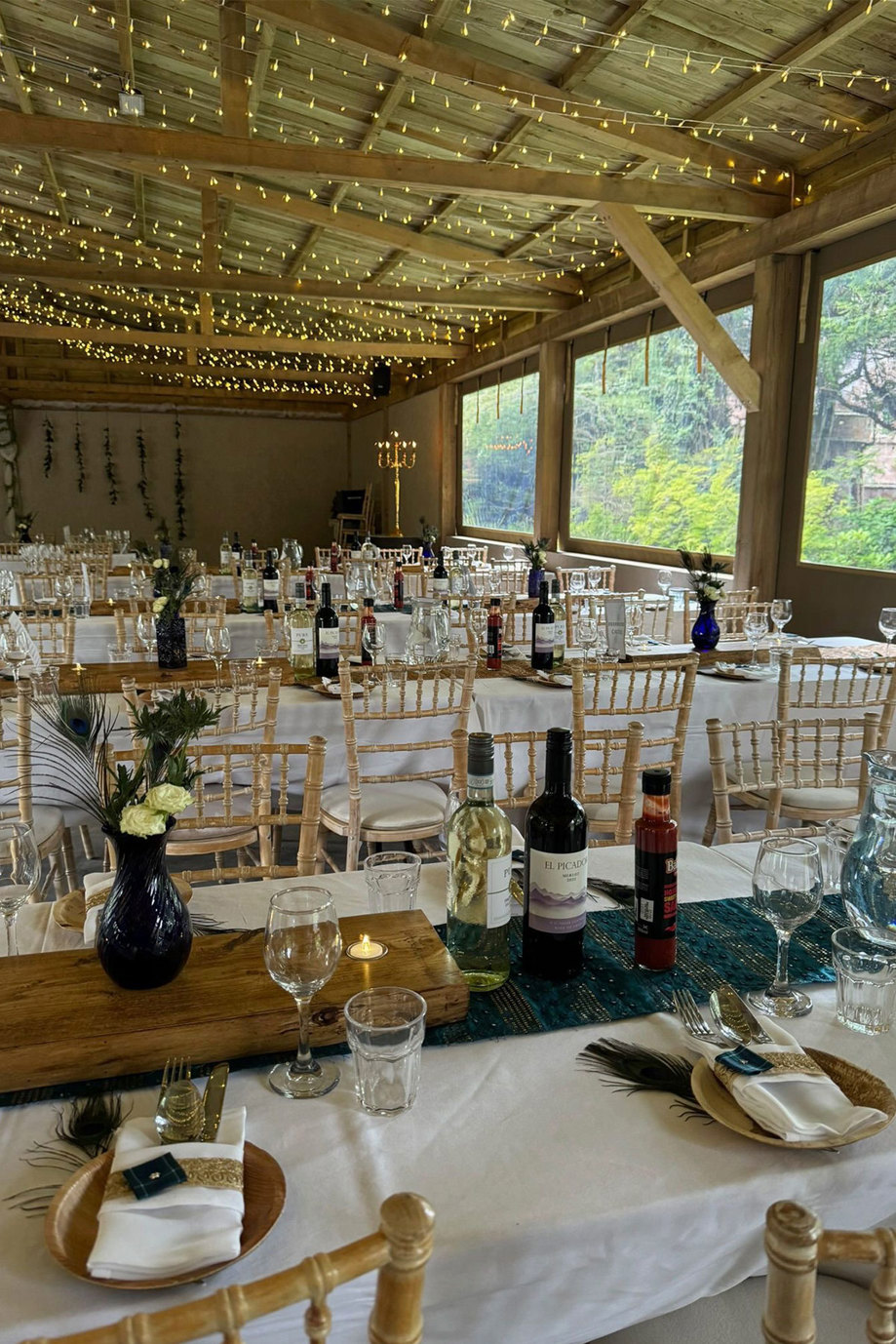 Inside a wooden barn with long tables set up for a meal and fairylights hanging from the roof