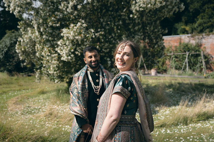 A bride and groom wearing Indian attire posing for a photo in the walled garden at Byre of Inchyra.