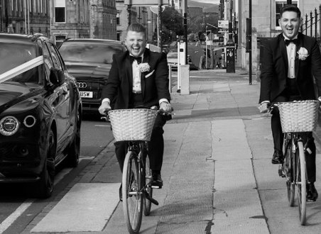 black and white picture of two grooms cycling through glasgow city centre