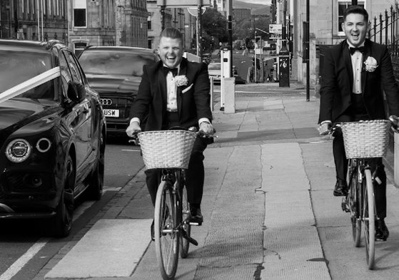 black and white picture of two grooms cycling through glasgow city centre
