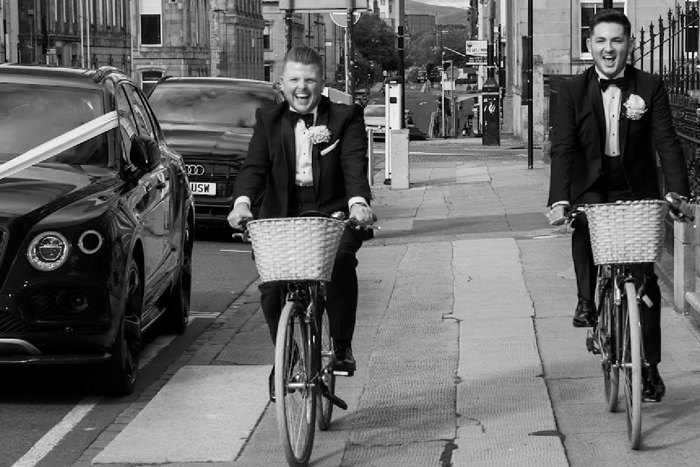 black and white picture of two grooms cycling through glasgow city centre