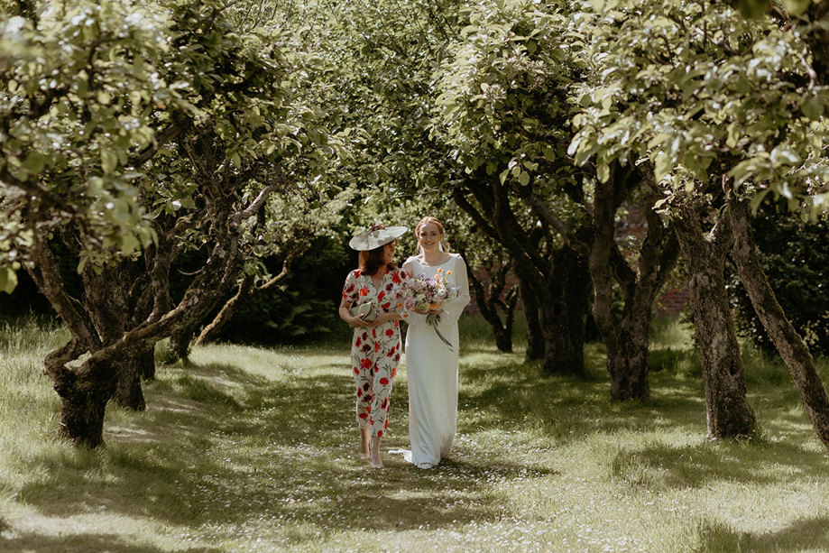 a bride walking down a natural outdoor aisle of trees on the arm of her mother at the Byre at Inchrya