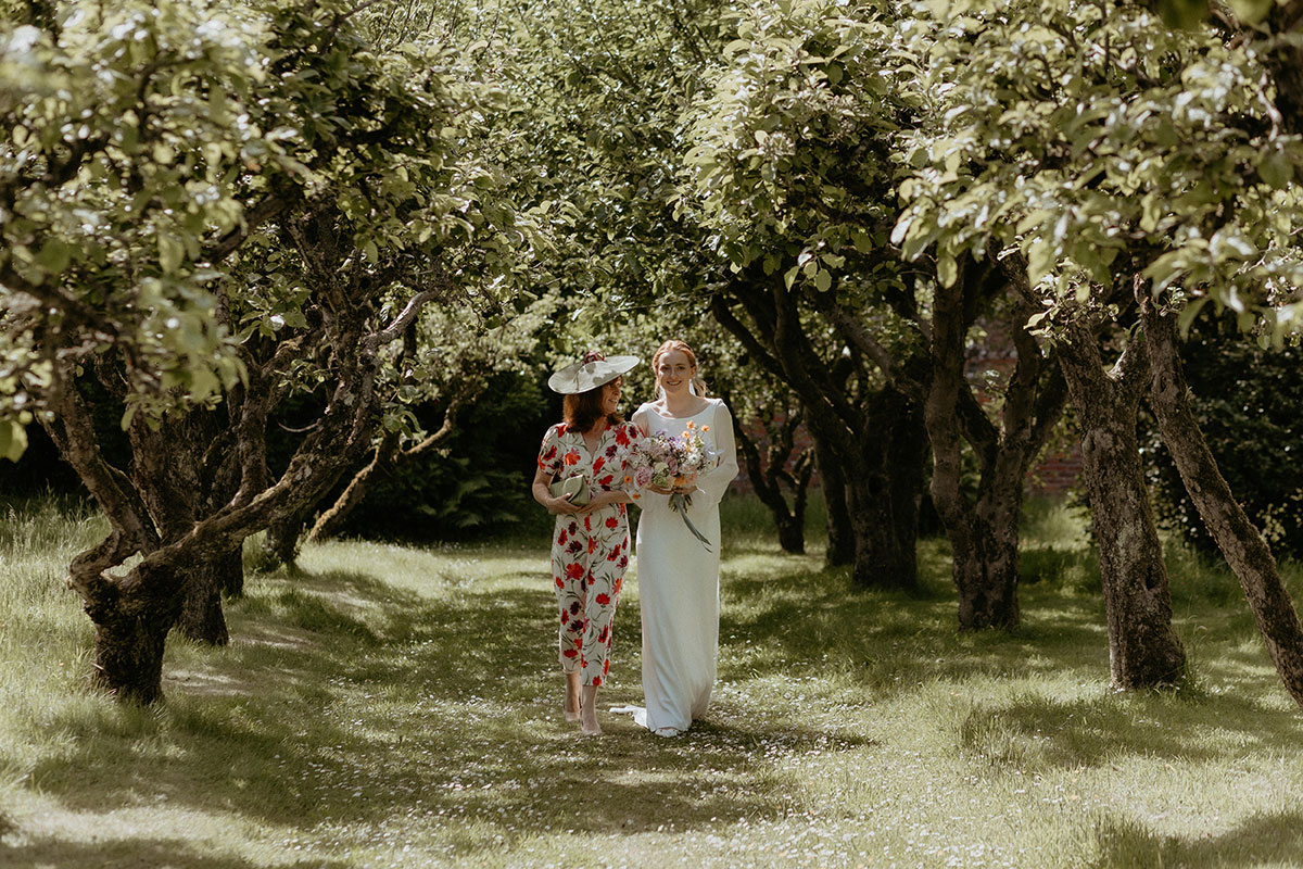 a bride walking down a natural outdoor aisle of trees on the arm of her mother at the Byre at Inchrya