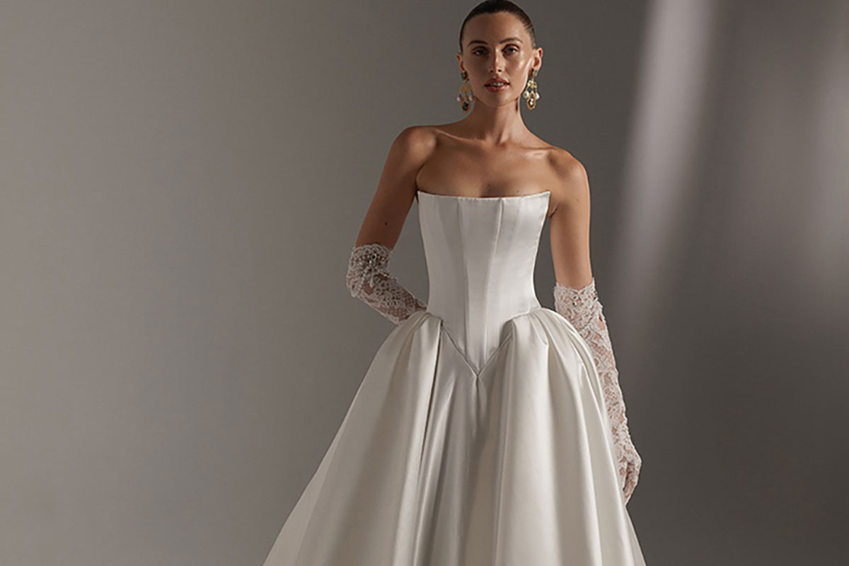 Model wearing a structured Berta wedding dress with a corseted bodice, full satin skirt and sheer lace gloves, photographed against a soft grey studio backdrop