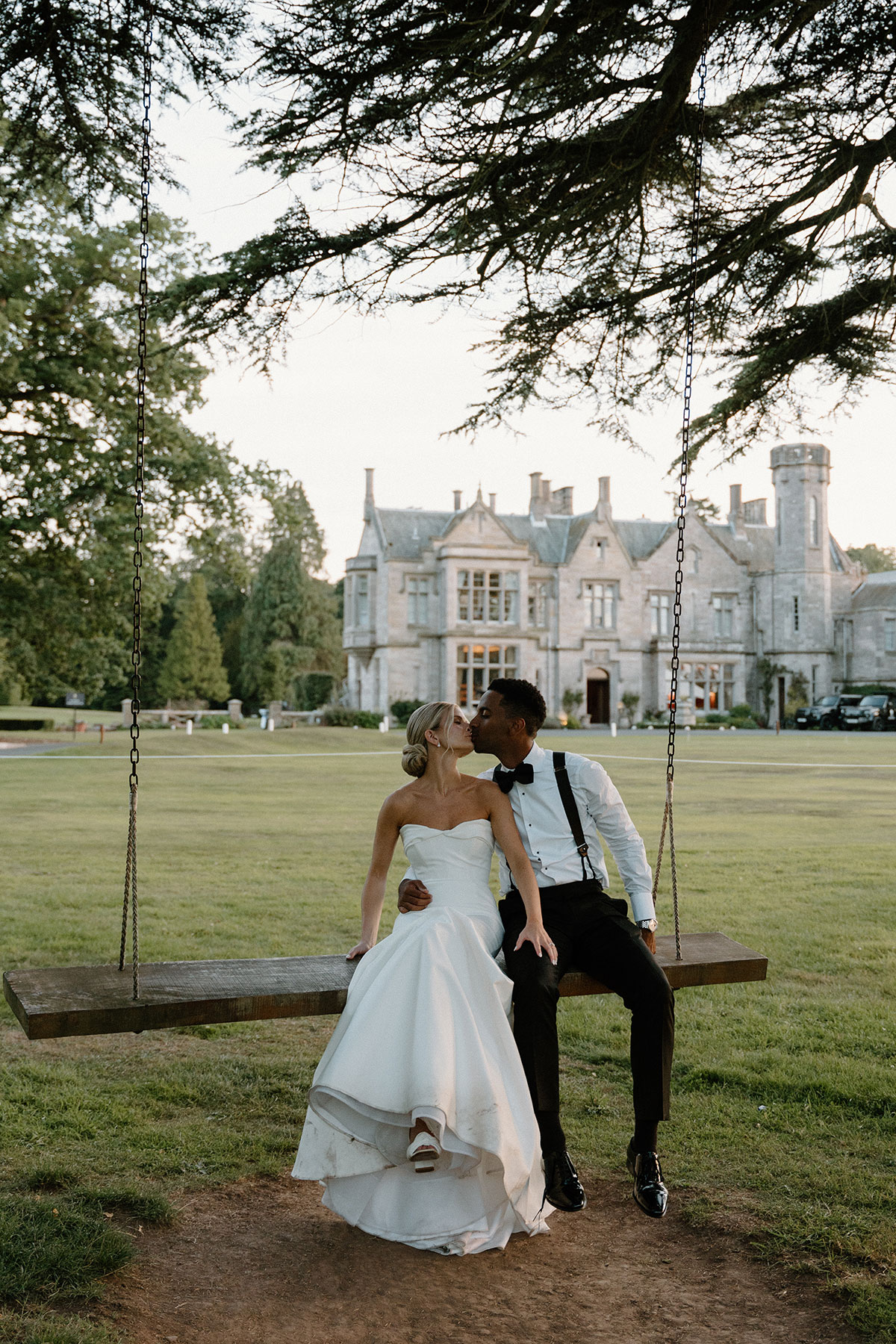 Newlywed couple kissing while sitting on a wooden swing in front of a Scottish castle wedding venue at dusk