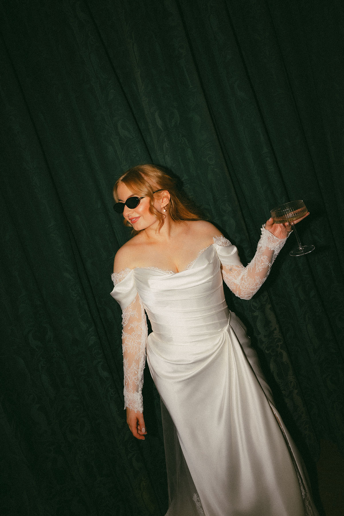 Bride wearing sunglasses holding champagne glass against dark backdrop at modern Scottish wedding reception