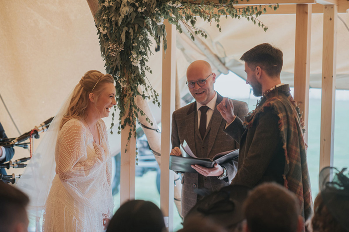Bride and groom laugh with officiant during their wedding ceremony