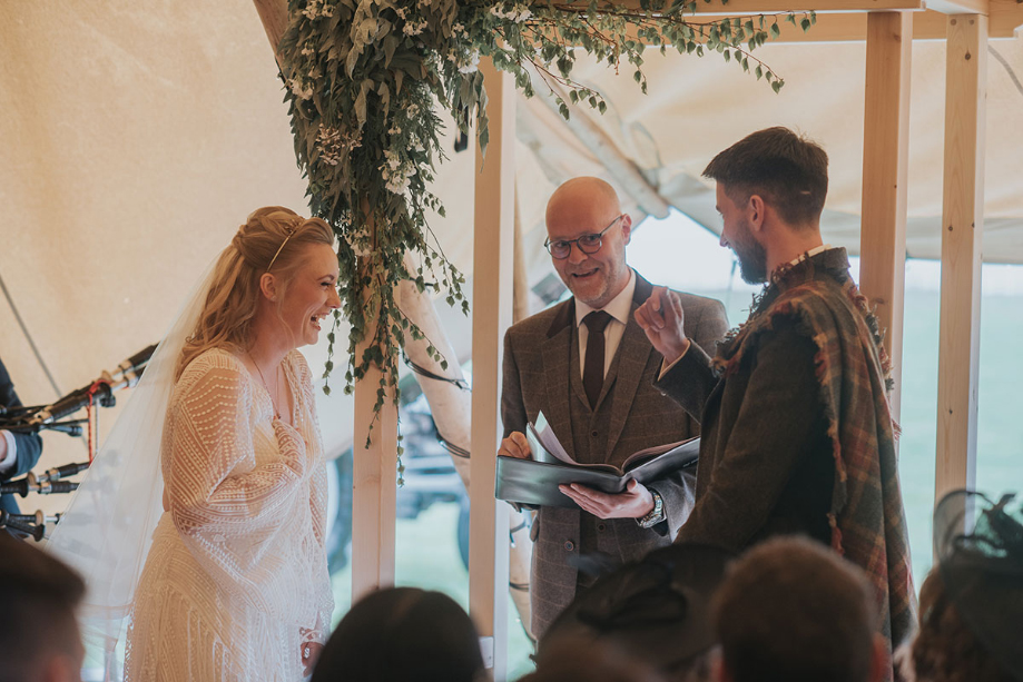 Bride and groom laugh with officiant during their wedding ceremony