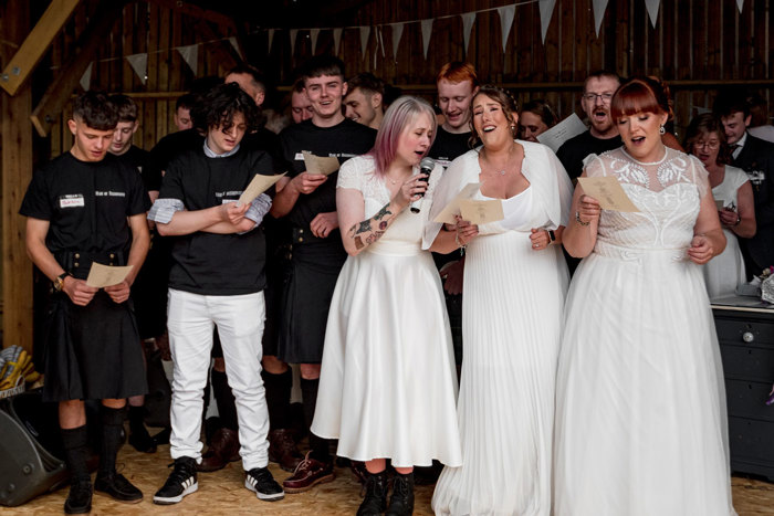 A Group Of People Dressed In Black And White Outfits Singing Holding Small Sheets Of Paper