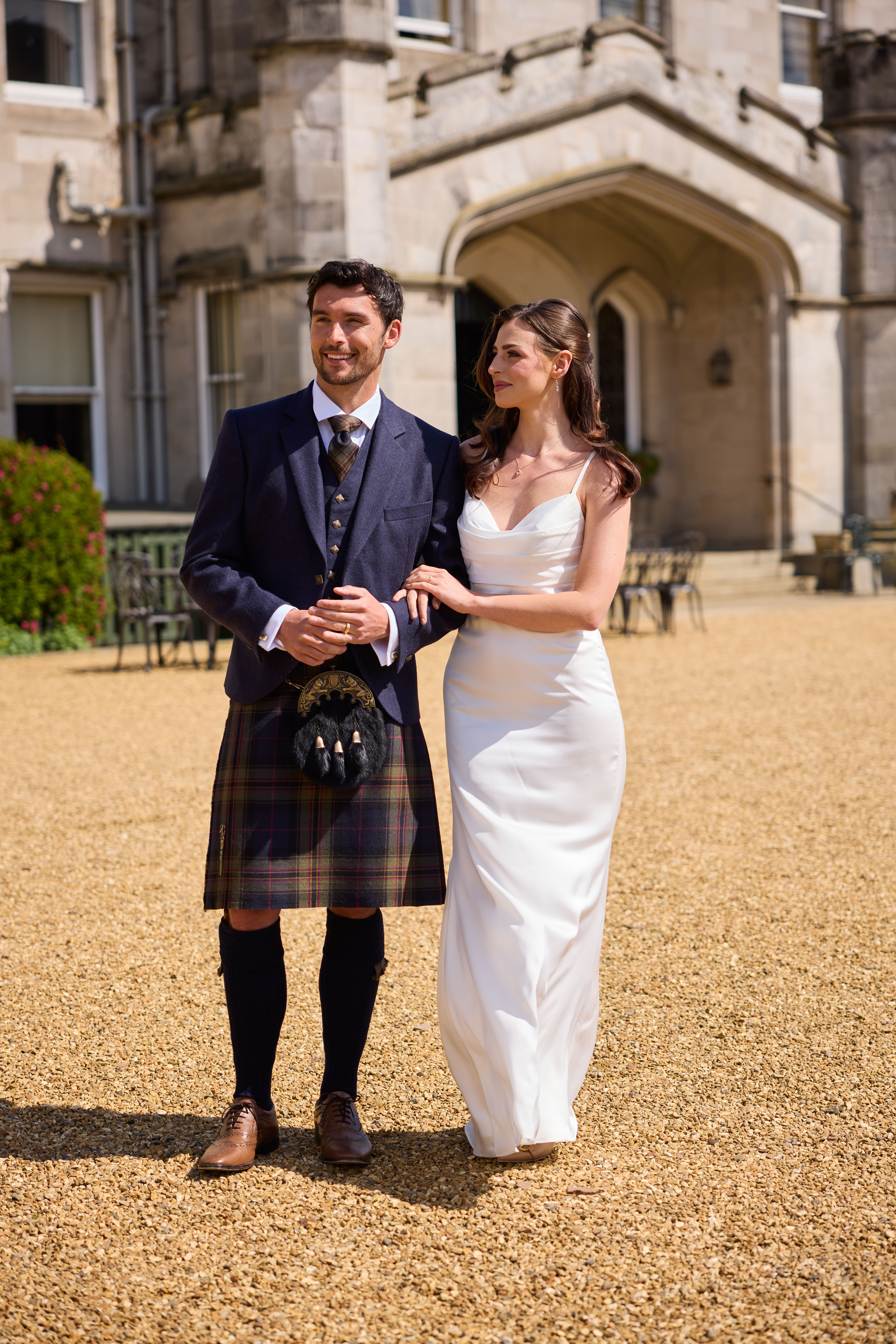 bride and groom smile and link arms in front of dundas castle as groom wears mccalls highlandwear's new noble print tartan kilt