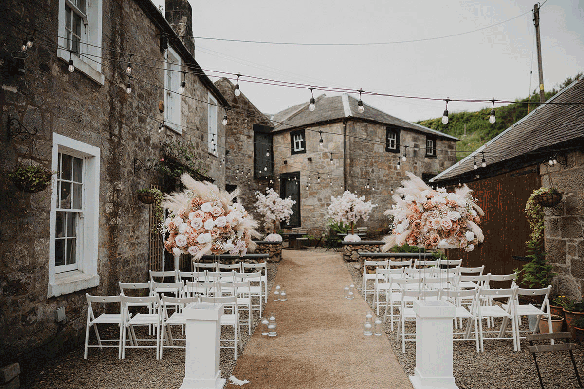 Old buildings with white chairs laid out in front and pink flowers