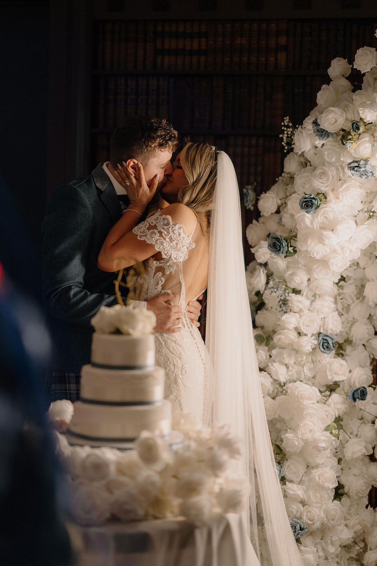 bride and groom kiss in front of wedding cake that has blue ribbon around each tier