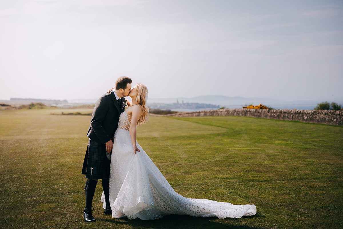 Bride and groom kissing on the grounds at Fairmont St Andrews with coastal views over St Andrews Bay