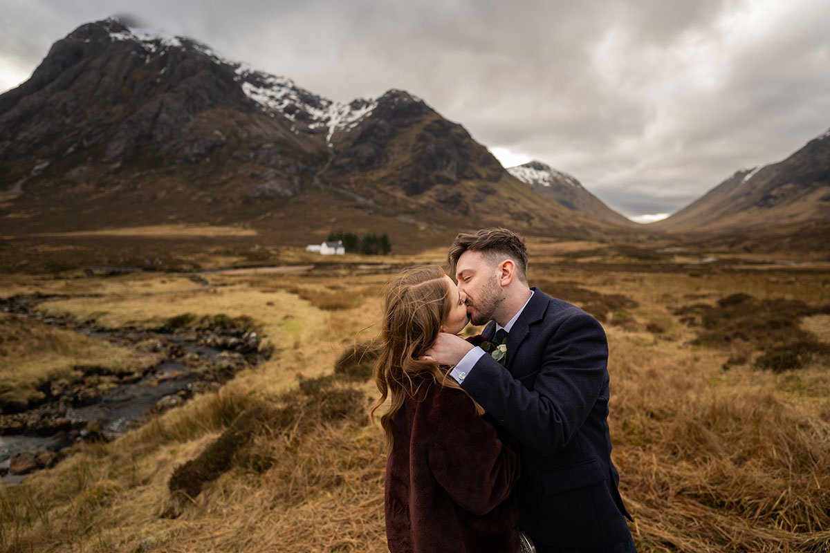 Bride and groom kissing in the dramatic Glencoe landscape after their Scottish elopement, surrounded by Highland mountains