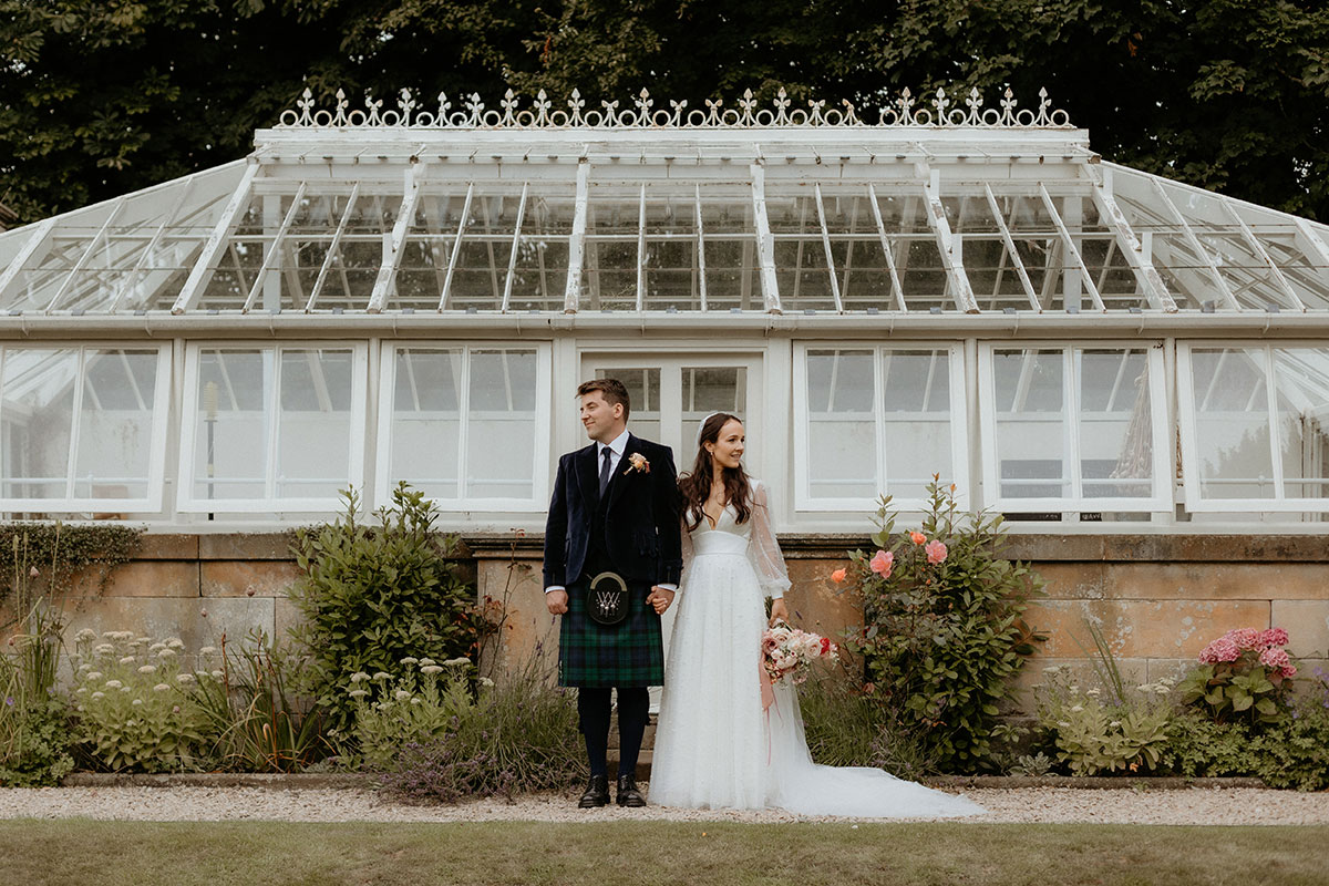 a bride and groom posing outside a white glasshouse at Carlowrie Castle
