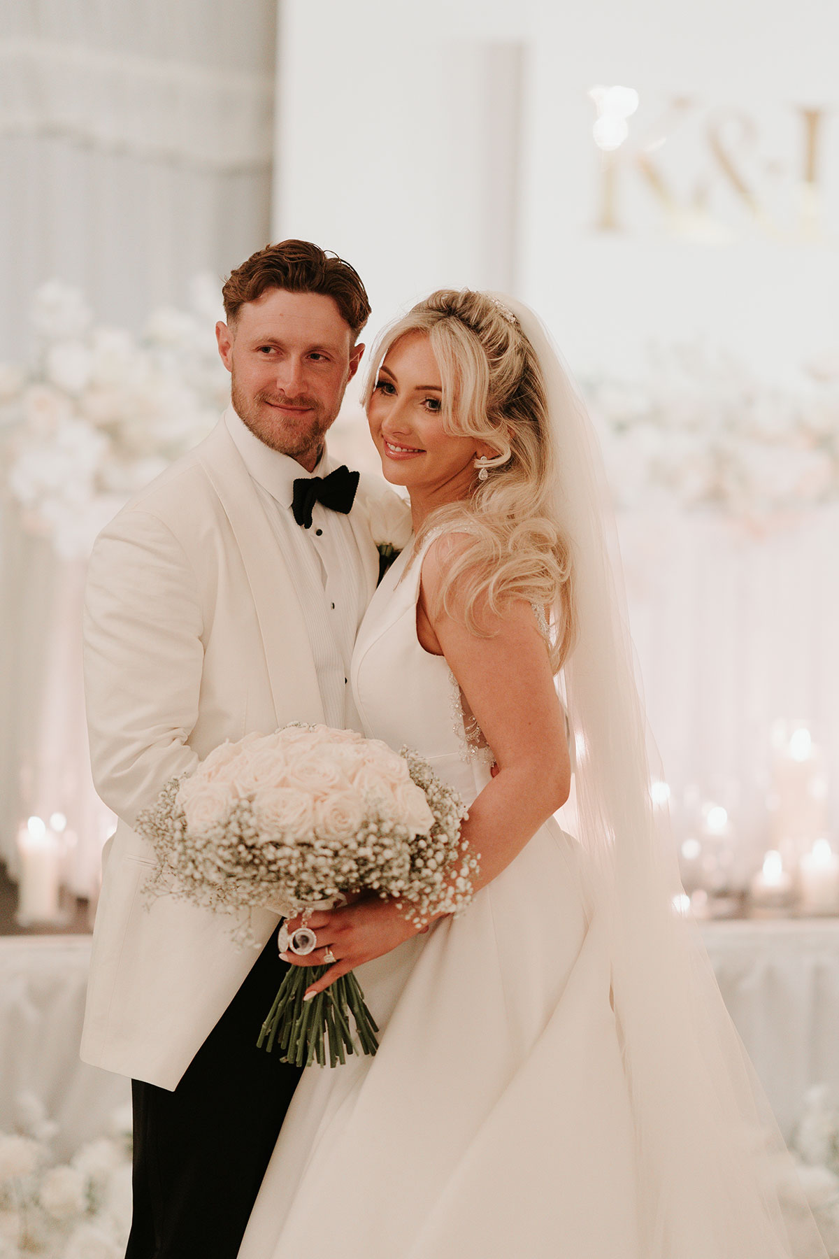 Newlyweds portrait with white rose bouquet and candlelit backdrop at Ingliston Country Club