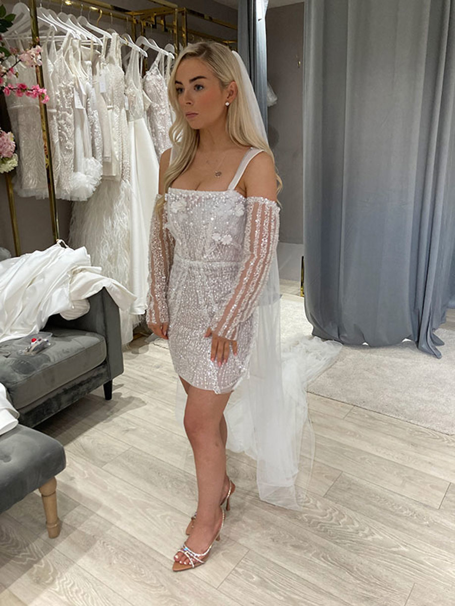 bride stands in boutique trying on a sparkly mini wedding dress with detachable matching sleeves and a long veil