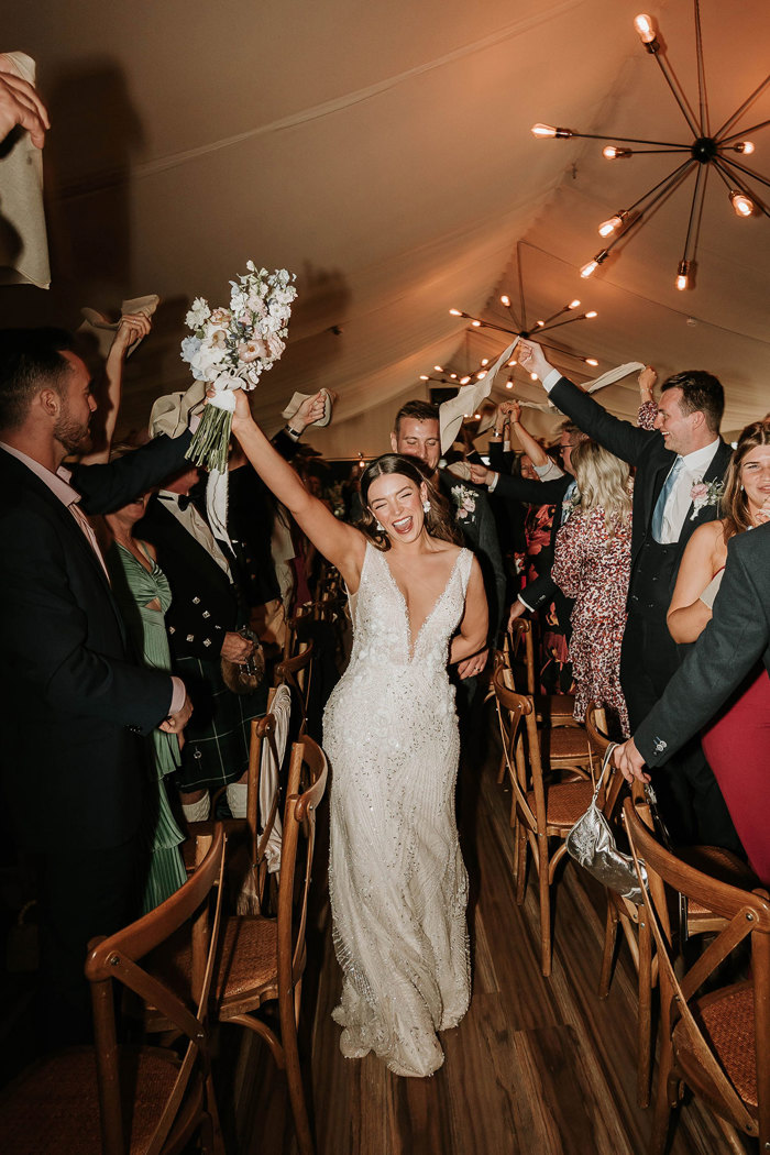 an elated bride and groom entering for dinner at Dunglass Estate amid two rows of standing guests waving napkins in the air