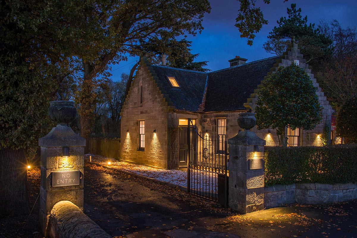 Carlowrie Castle gatehouse at dusk, with stone exterior, illuminated entrance and gated courtyard