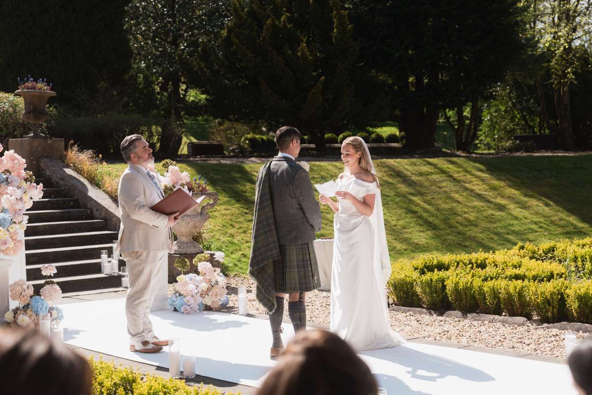 Siân and Stuart exchange personal vows during their outdoor wedding ceremony in the gardens at Mar Hall, Renfrewshire.
