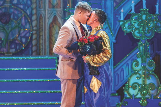 Two men kissing on stage holding red roses