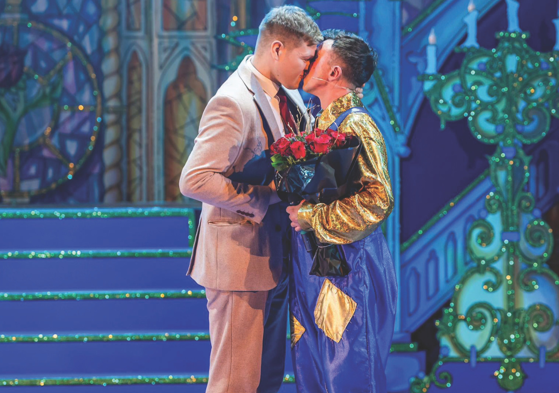 Two men kissing on stage holding red roses