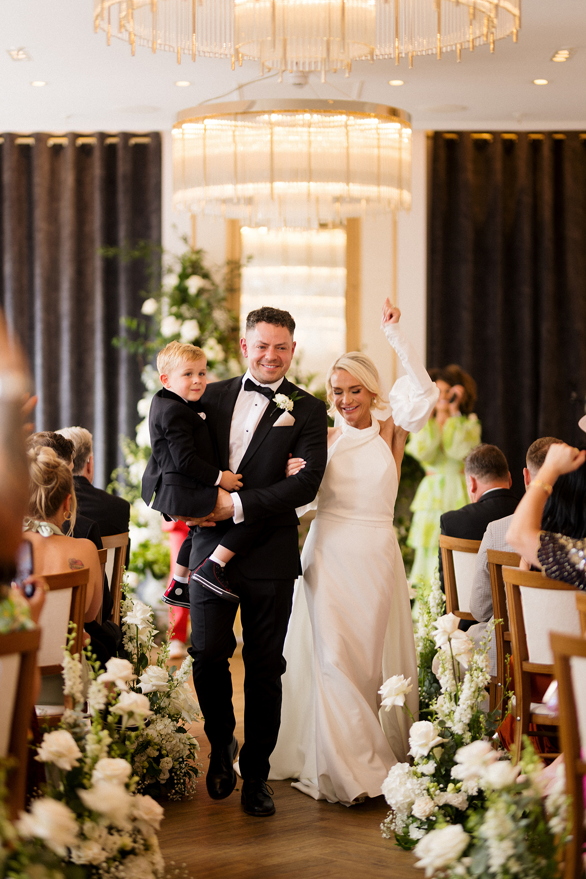 Bride and groom walking back down the aisle with a young child after their ceremony