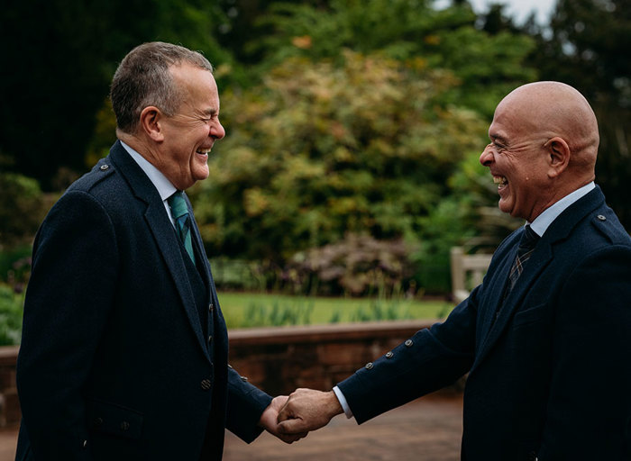 two grooms smile and hold hands during their first look in the ornamental garden at Brodick Castle 