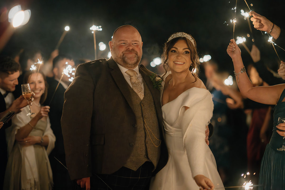 Newlywed bride and groom smiling with sparklers during their evening celebration at Cluny Castle.