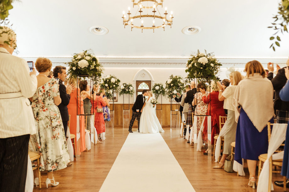 bride and groom stand at the top of aisle with guests cheering during wedding at crossbasket castle