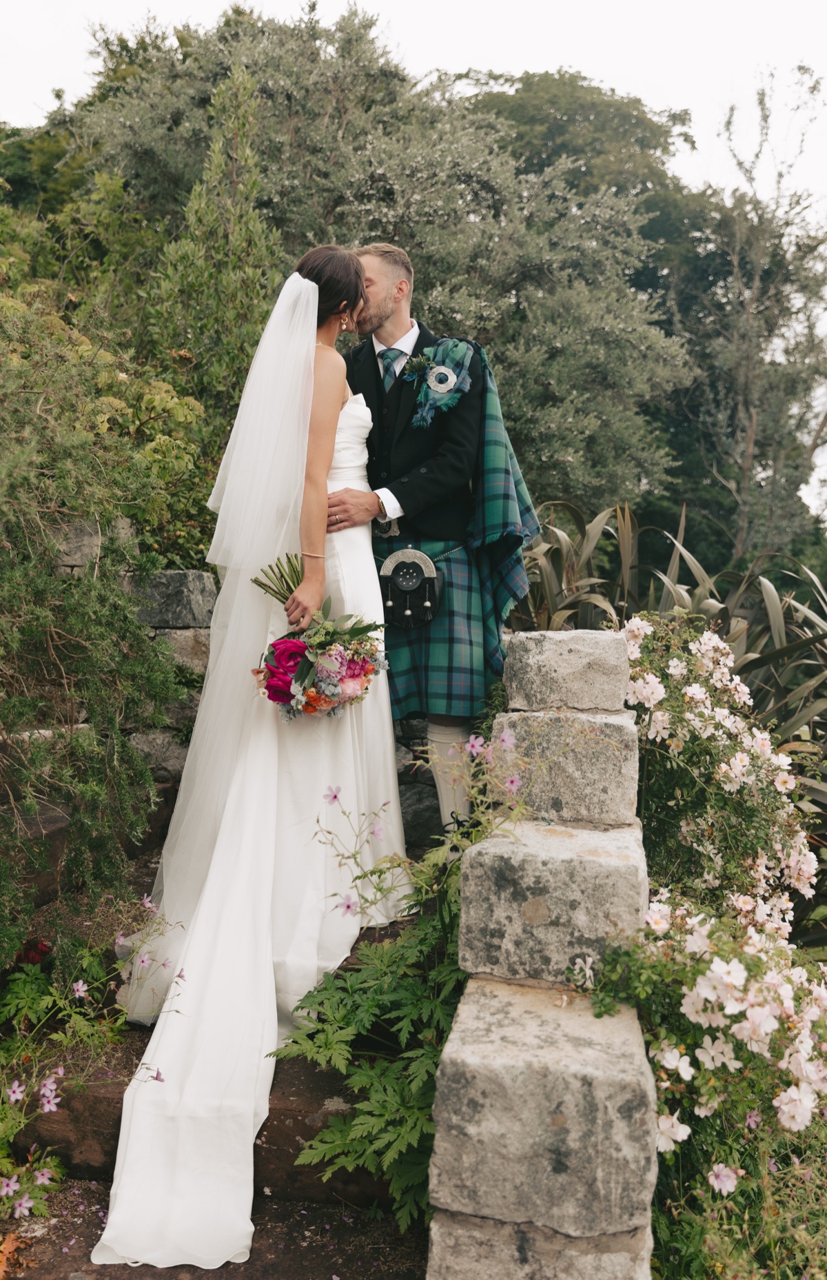 Isobel and Gary kiss among flowers and greenery during their Isle of Arran wedding portraits.