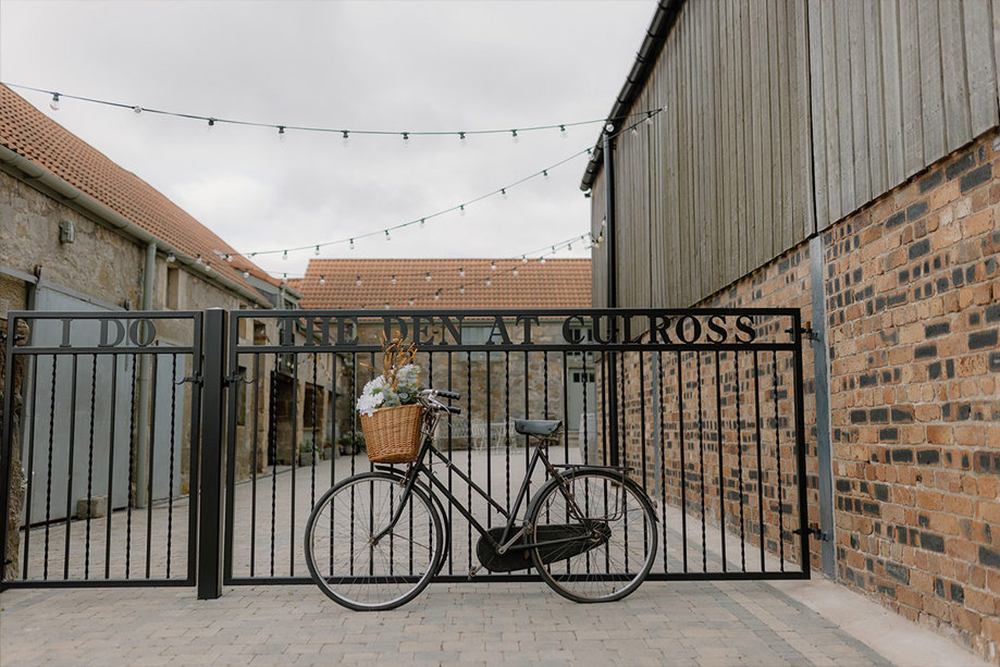 a boke with a basket of flowers in the front propped against a black gate that included the words 'The Den At Culross'