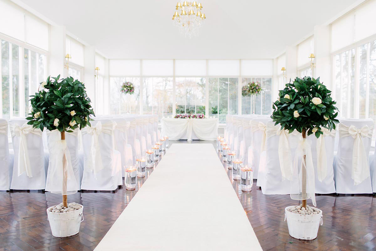 Carlowrie Castle Orangery set for a wedding ceremony with white chairs, floral arrangements and candle-lined aisle