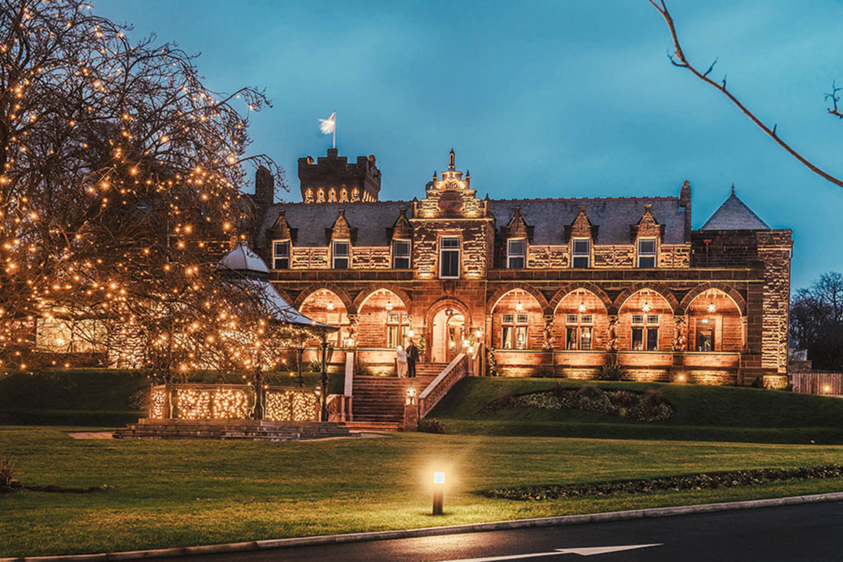 large brick house with grand entrance steps and a gazebo on the lawn are both lit up with warm and twinkling lights