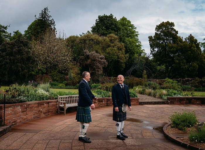 two grooms wearing kilts having a first look in the ornamental garden at Brodick Castle on their wedding day 