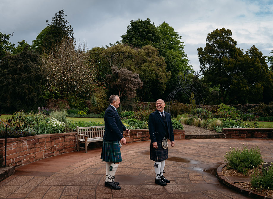 two grooms wearing kilts having a first look in the ornamental garden at Brodick Castle on their wedding day