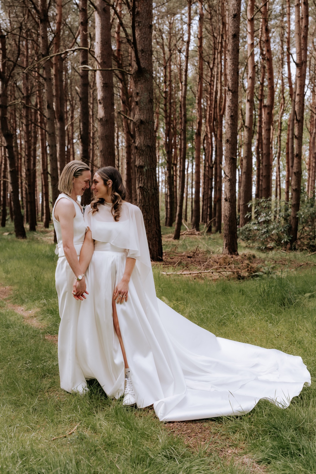 Hannah and Donna standing together hand in hand during their woodland wedding portraits at Harvest Moon.