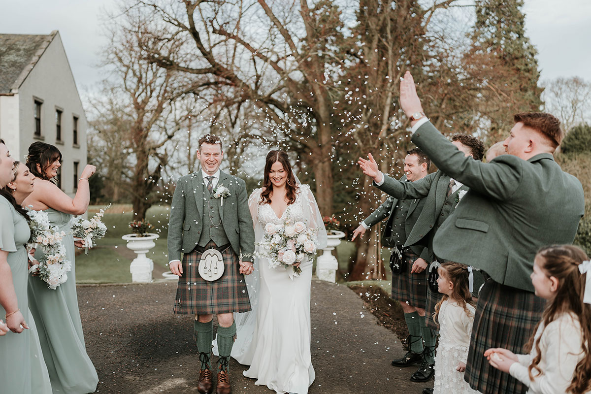 Bride and groom smiling during confetti throw with bridesmaids and groomsmen